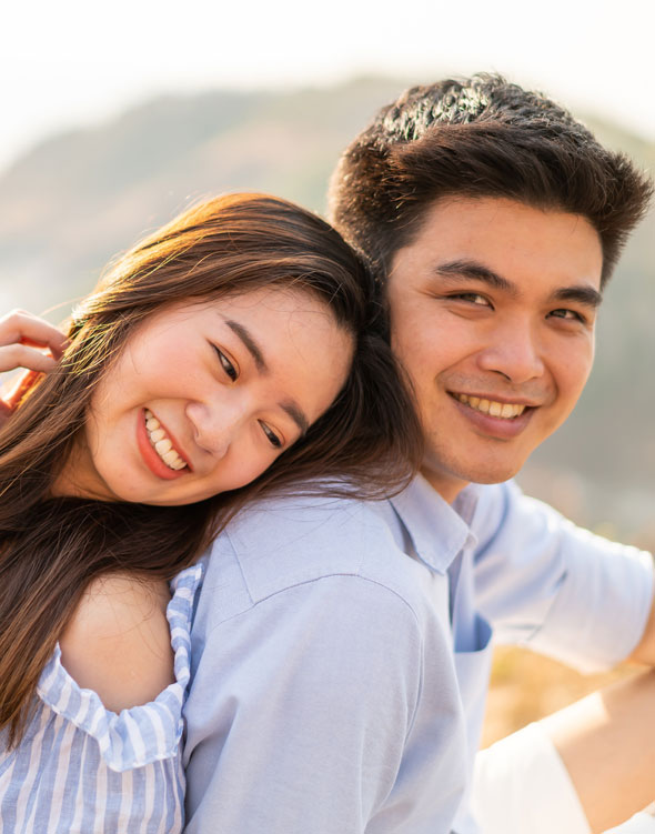 Asian couple sitting back to back and smiling at the camera